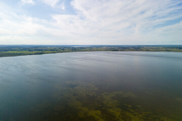 Aerial view of a tranquil lake surrounded by lush green fields under a blue sky with wispy clouds. Perfect for nature and landscape themes.