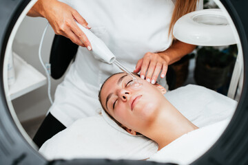 Obraz premium Young woman receiving face lift treatment with high-frequency wand. This modern treatment uses electric currents to kill acne-causing bacteria, reduce inflammation, and improve skin tone and texture.
