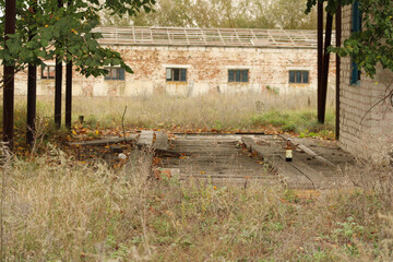 Fototapeta premium A dilapidated structure with remnants of old construction materials scattered around, emphasizing its state of disrepair amidst tall grass and weeds