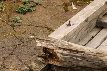 A concrete structure with a rusty nail protruding from it, surrounded by wooden debris and rough textures