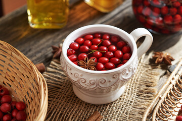 A cup of herbal tea with fresh hawthorn berries on a table in autumn