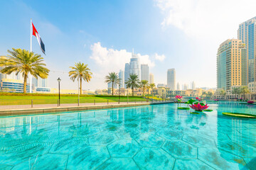 Colorful lily pad flowers artwork in the turquoise water of the Dubai Fountain, with the skyline, Emirates flag and Dubai mall in view, in Dubai, United Arab Emirates.