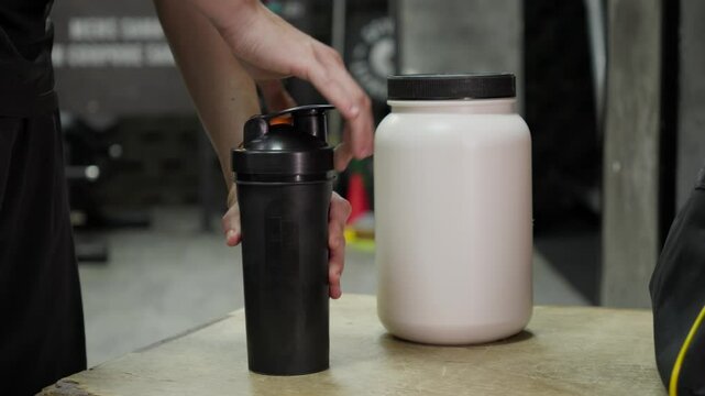 Preparing a Protein Shake in the Gym with Whey Protein. Close-up of a person preparing a whey protein shake in the gym, ideal for supplement commercials and fitness nutrition content.