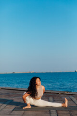 Athletic woman doing gymnastics yoga asana by the sea