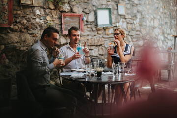 Three friends relax and enjoy colorful cocktails at an outdoor cafe, creating a lively and social atmosphere against a rustic stone wall.