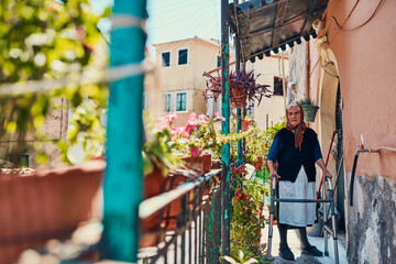 Naklejka premium Portrait, senior woman and walker in home on front porch in ancient architecture with garden. Pensioner, person with a disability and retirement for mobility, balance and support for walking in Italy