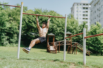 Fit man exercising on a pull-up bar in an outdoor park. Fitness and strength training in nature on...