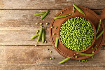 Fresh green peas in bowl and pods on wooden table, flat lay. Space for text