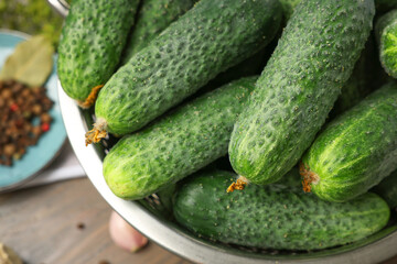 Fresh green cucumbers in colander on table, closeup