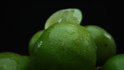 Slices of lime are meticulously arranged in a pile, set against a black background. Each lime slice is captured in stunning detail, its vibrant green hue and enticing texture. Close up. Comestible.