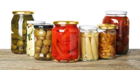 Different pickled products in jars on wooden table against white background