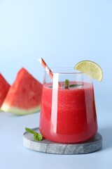 Tasty watermelon drink in glass, mint and fresh fruits on light blue background