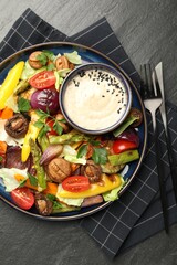 Delicious salad with grilled vegetables and sauce served on dark gray textured table, flat lay