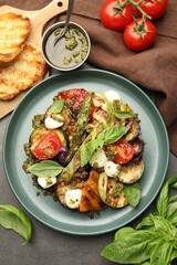 Delicious salad with grilled vegetables, pesto sauce, basil and bread on gray textured table, flat lay