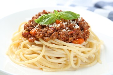 Tasty pasta bolognese with basil on white plate, closeup