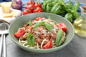 Delicious pasta bolognese with basil and tomatoes served on grey table, closeup
