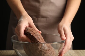 Woman kneading chocolate dough at wooden table, closeup