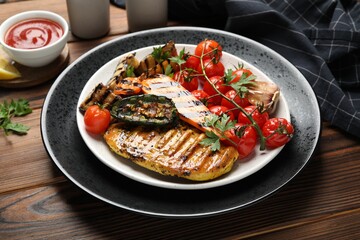 Delicious grilled vegetables and chicken breast on wooden table, closeup