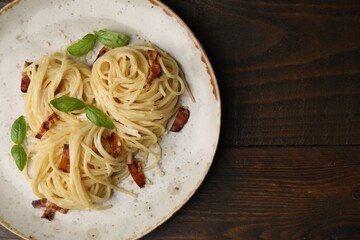 Delicious pasta with bacon and basil on wooden table, top view. Space for text
