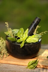 Fresh herbs. Basil leaves in mortar on wooden table outdoors, closeup
