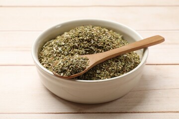 Dried oregano in bowl and spoon on wooden table, closeup