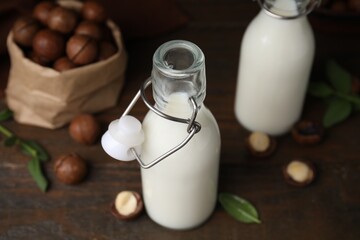 Bottles of macadamia milk and nuts on wooden table, closeup
