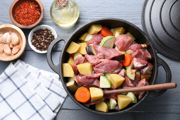 Uncooked meat and vegetables in pot on light grey wooden table, flat lay