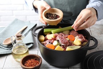 Woman preparing stew with vegetables and meat at white tiled table, closeup