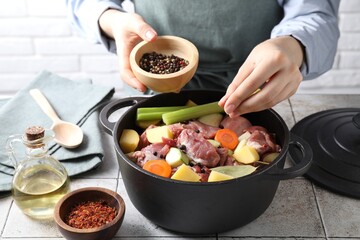 Woman preparing stew with vegetables and meat at white tiled table, closeup