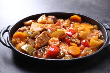 Delicious stew with vegetables in baking dish on grey table, closeup