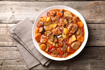 Delicious stew with vegetables in bowl on wooden table, top view