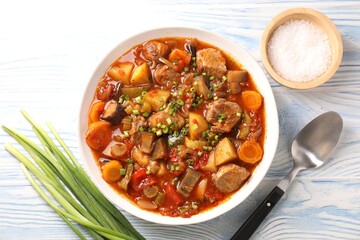 Delicious stew with vegetables in bowl, spices and spoon on light blue wooden background, top view