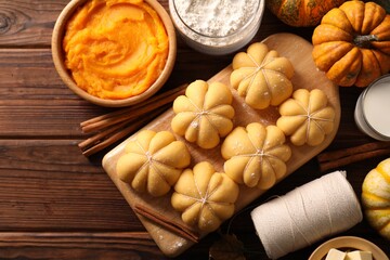Raw pumpkin shaped buns and ingredients on wooden table, flat lay