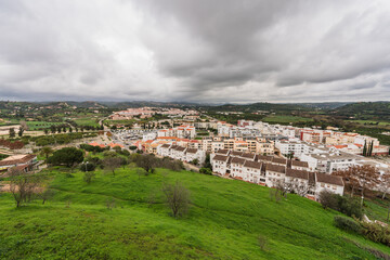 Storm clouds gather above a sprawling Portuguese town, nestled among verdant hills.