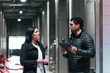 Caucasian couple during the winery visit, walking through the production industry cellar using a tablet to know the process of the winemaking