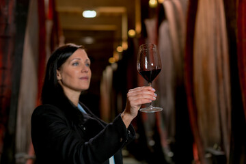 Woman tasting wine at the wine cellar with barrels in background