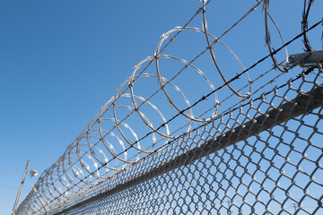 Barbed wire on the fence. Barbed wire fence delimiting the border of safe area. Security, protection, and boundaries. Barbed wire hedgehog and electric fence. Territory protection wire.
