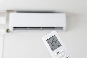 Adjusting air conditioner temperature with remote control. Hand holds remote control and setting comfortable temperature on climate system in apartment