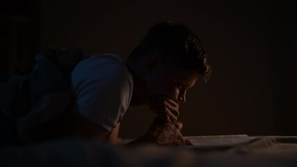 Young man engrossed in book, illuminated by warm lamp light, while reading in bed at night, showing his deep interest in the story. Serene male reading book lying in bed at night, bathed in soft light