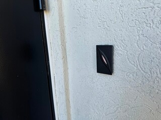 A small black switch on a textured white wall next to a door frame