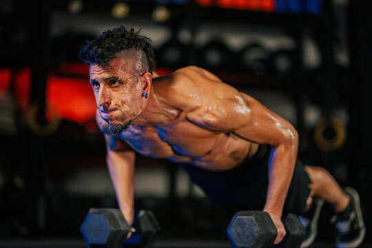 Portrait of a sweaty shirtless man doing pushups or plank with weights in a gym - Powered by Adobe