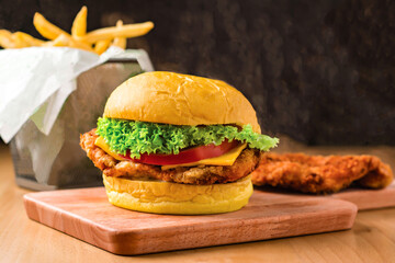 Crispy Chicken Burger with Lettuce, Jalapeno, Tomato, Cheese isolated on wooden board with french fries basket side view of fastfood