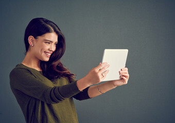 Naklejka premium Happy, woman and tablet in studio for video call, live stream and connectivity to internet. Influencer, smile and tech on gray background for selfie, follower interaction and social media update