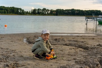 Little boy playing alone on the beach by the water with toy cars. Concept of child safety near water bodies and outdoor playtime. High quality photo