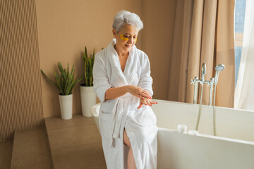 Mature adult old woman applying moisturizing body lotion on hands. Senior lady rubbing nourishing...