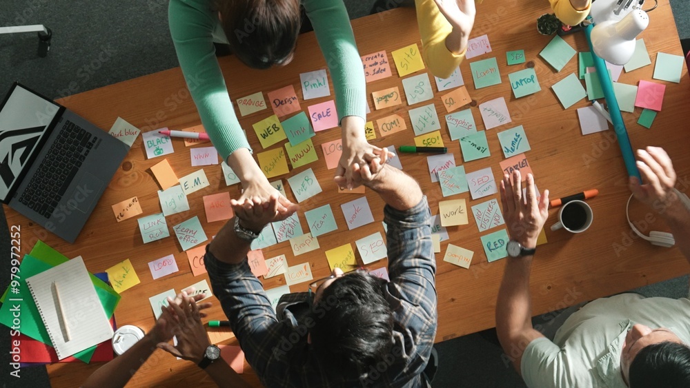 Poster top view of business team giving high five to celebrate project while standing at table with sticky 