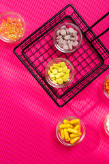 Different pills and tablets of dietary supplements in small glass bowls from above on a pink background in sun rays. Groups of vitamins and minerals top view.