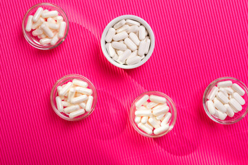Dietary supplements pills in white colour from above on a pink background.