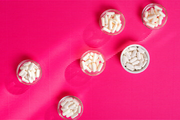 Dietary supplements pills in white colour from above on a pink background.
