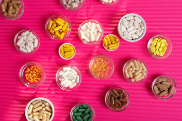 Dietary supplements, vitamins and minerals in form of colourful pills, tablets, capsules in small round bowls on a pink background in sun light top view. 